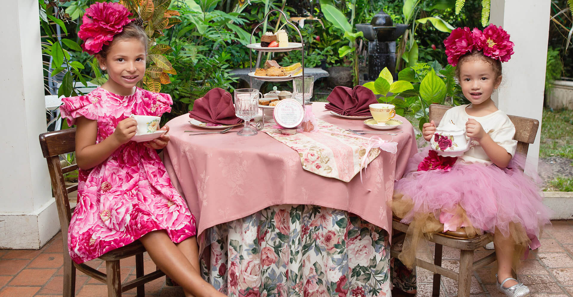 Two kids wearing pink floral dresses and having tea